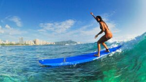 close up of woman on blue surf board in the water with city skyline in background